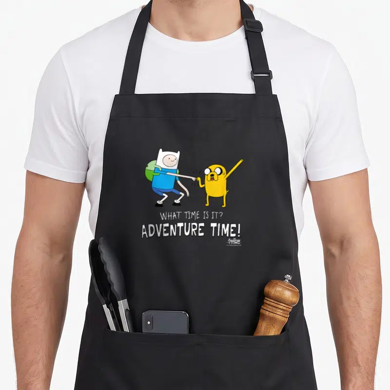 Tablier de cuisine noir avec Finn et Jake se faisant un poing et le texte What time is it Adventure Time imprimé en blanc.