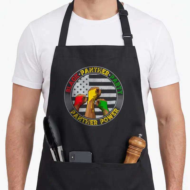 Tablier de cuisine noir avec logo circulaire Black Panther Party et trois poings fermés peints en rouge, jaune et vert.
