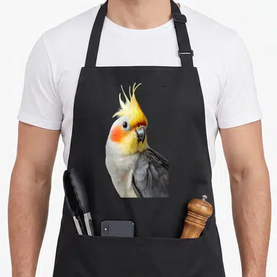 Tablier de cuisine noir avec une calopsitte aux plumes grises, jaunes et marques orangées sur les joues.