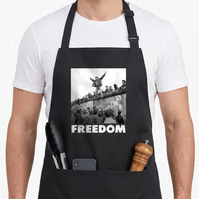 Tablier de cuisine noir avec photo historique sur un mur et le mot FREEDOT en bas.