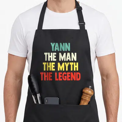 Tablier de cuisine noir avec le texte Yann The Man The Myth The Legend en lettres multicolores.