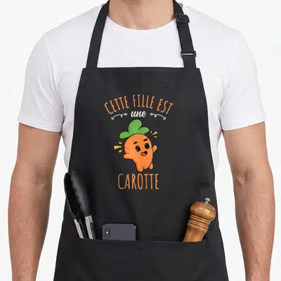 Tablier de cuisine noir avec une carotte souriante et le texte Cette Fille Est Une Carotte imprimé en orange et blanc.