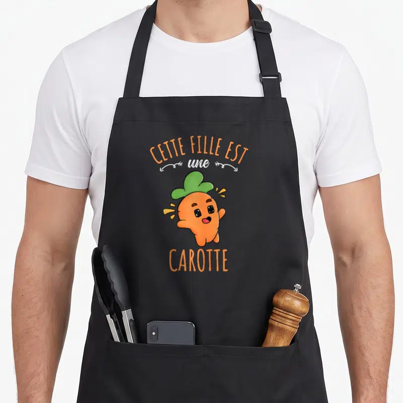 Tablier de cuisine noir avec une carotte souriante et le texte Cette Fille Est Une Carotte imprimé en orange et blanc.