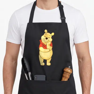 Tablier de cuisine noir avec Winnie l'ourson jaune en chemise rouge posant la main sur sa bouche.