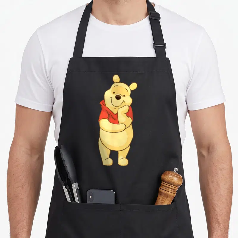 Tablier de cuisine noir avec Winnie l'ourson jaune en chemise rouge posant la main sur sa bouche.