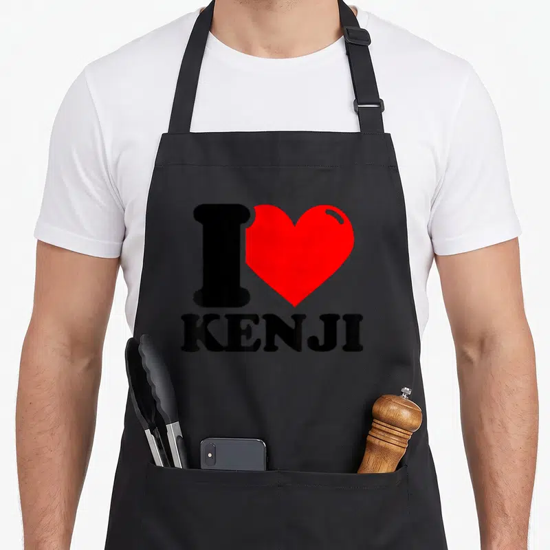 Tablier de cuisine noir avec un grand cœur rouge et le texte J'ADORE KENJI en lettres noires capitales au centre.