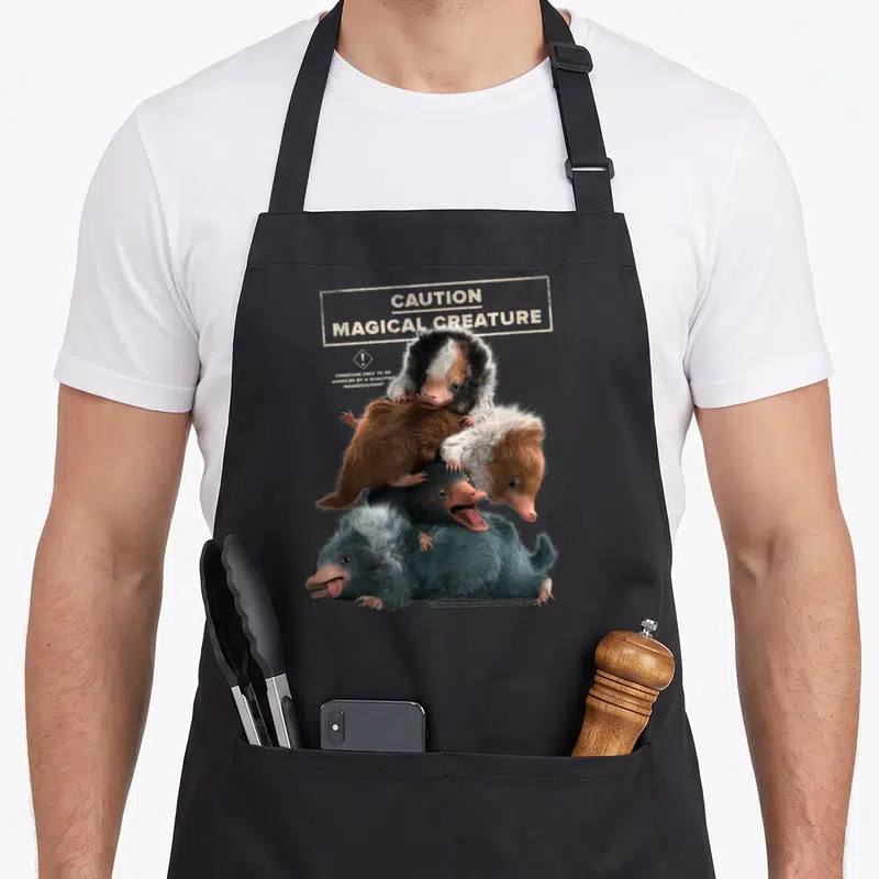 Tablier de cuisine noir avec une illustration de quatre Nifflers empilés et un avertissement en anglais.