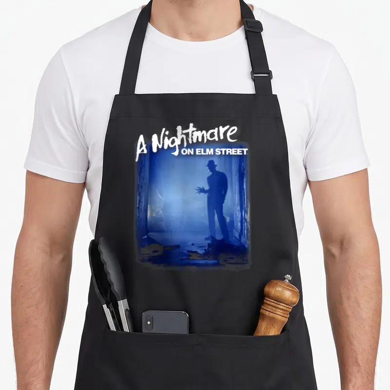 Tablier de cuisine noir avec une silhouette bleue de Freddy Krueger et le texte A Nightmare on Elm Street Freddy Is Waiting.