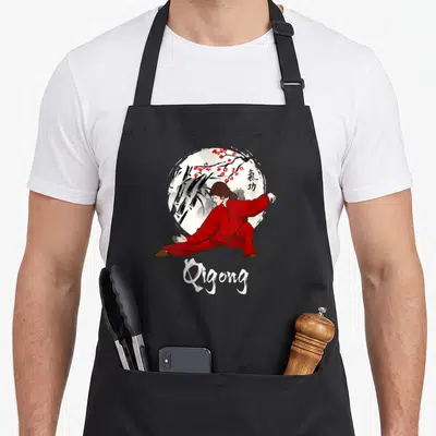 Tablier de cuisine noir avec une femme en tenue rouge pratiquant le Qigong devant un cercle blanc et des fleurs rouges.
