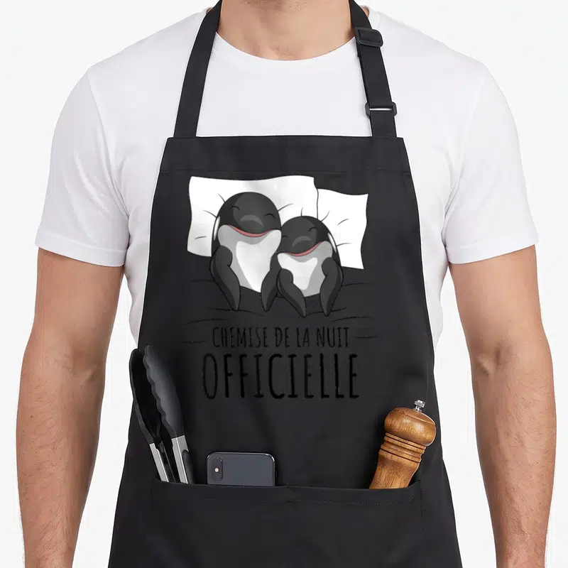 Tablier de cuisine noir avec deux orques souriants au lit et le texte Chemise de la nuit imprimé en noir.