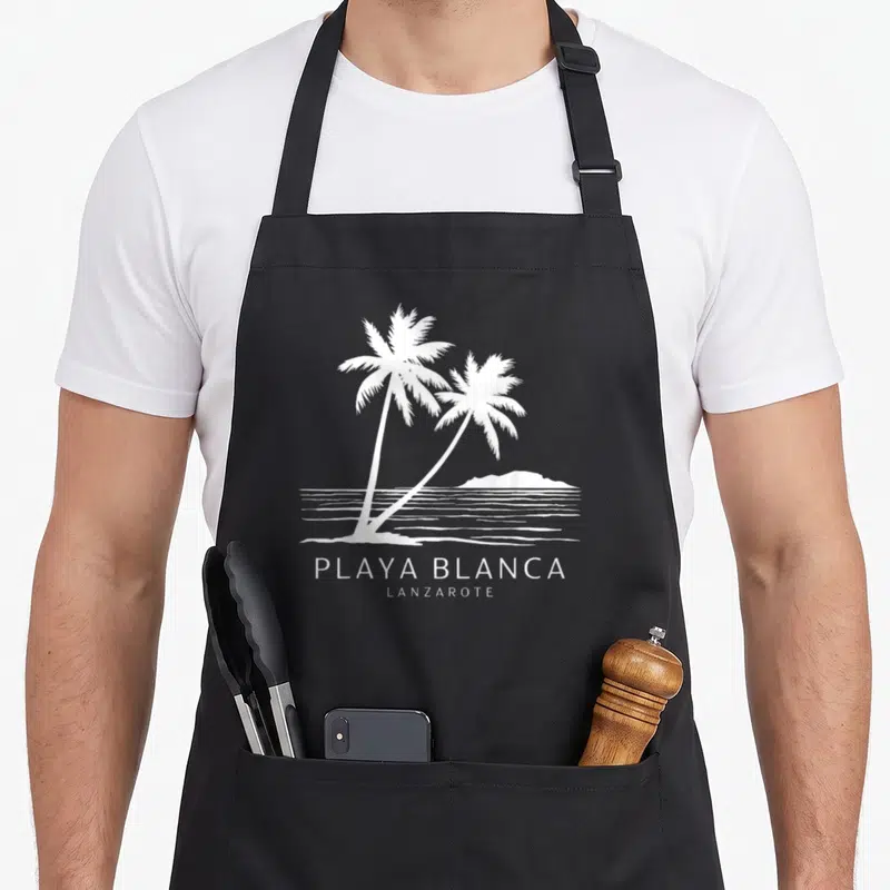 Tablier de cuisine noir avec illustration blanche de deux palmiers et l'inscription Playa Blanca Lanzarote au-dessus de lignes marines.