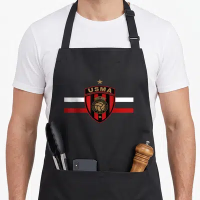 Tablier de cuisine noir avec l'écusson rouge et noir de l'USMA Union Sportive de la Médina d'Alger sur fond blanc et rouge.