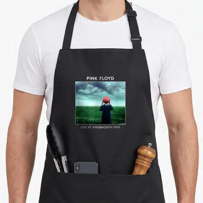 Tablier de cuisine noir avec illustration d'un homme tenant une balle rouge sous un ciel menaçant au-dessus d'une prairie verte.