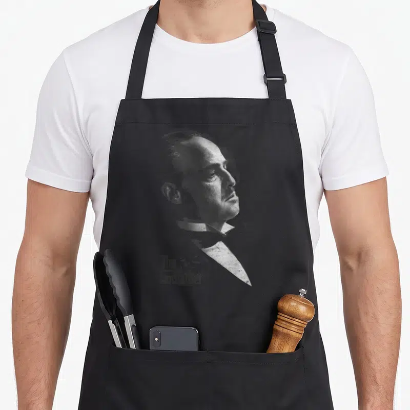 Tablier de cuisine noir avec portrait gravure de Vito Corleone et logo The Godfather en bas à gauche.