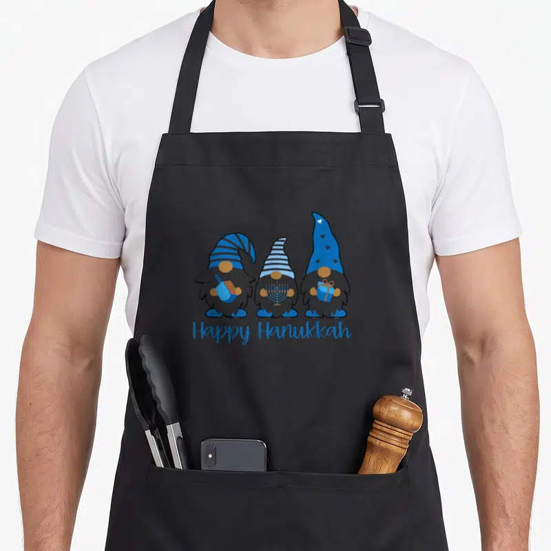 Tablier de cuisine noir avec trois nains de Hanoucca bleus et gris tenant un dreidel, une menorah et un cadeau sous l'inscription Happy Hanukkah.