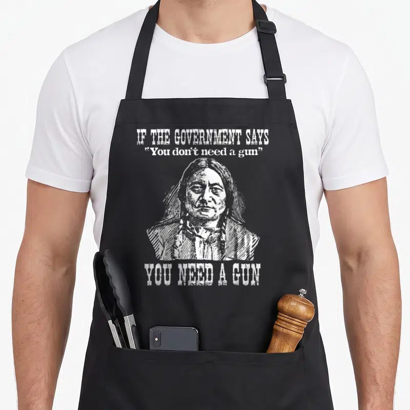 Tablier de cuisine noir avec illustration de Sitting Bull et texte You Need a Gun en blanc.