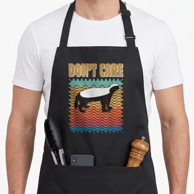 Tablier de cuisine noir avec illustration rétro d'un honey badger sur fond de vagues colorées et texte doré.