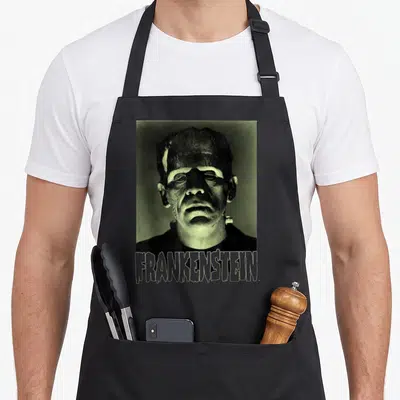 Tablier de cuisine noir avec portrait vert pâle de Frankenstein et texte FRANKENSTEIN en bas.