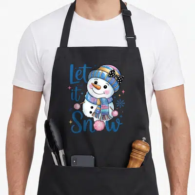 Tablier de cuisine noir avec un bonhomme de neige souriant portant une écharpe multicolore et le texte Let it Snow en bleu.