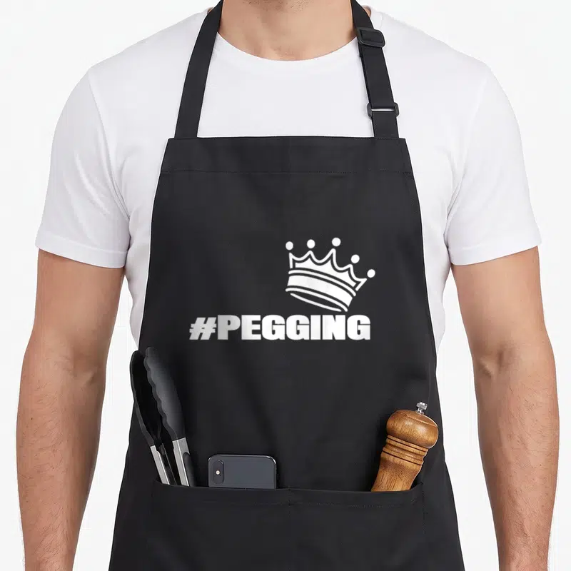 Tablier de cuisine noir avec une couronne blanche et le texte #PEGGING imprimé au centre.
