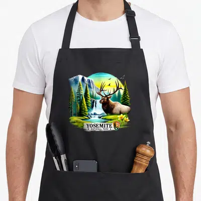 Tablier de cuisine noir avec illustration colorée d'un cerf devant une cascade et des pins au Yosemite National Park.