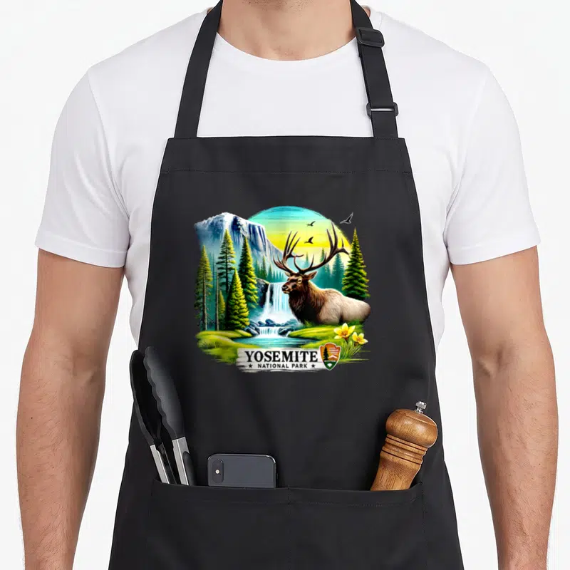 Tablier de cuisine noir avec illustration colorée d'un cerf devant une cascade et des pins au Yosemite National Park.
