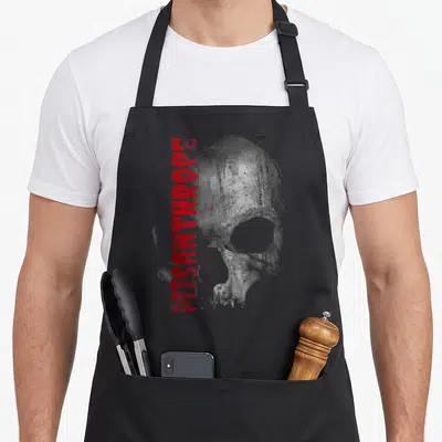 Tablier de cuisine noir avec un crâne gris texturé et l'inscription MISANTHROPE en lettres rouges verticales sur le côté gauche.