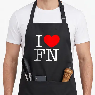 Tablier de cuisine noir avec l'inscription J'aime FN et un grand cœur rouge au centre du design imprimé.