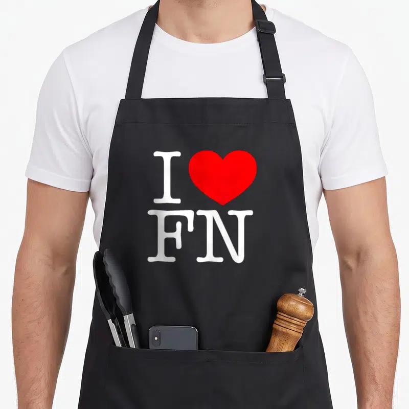 Tablier de cuisine noir avec l'inscription J'aime FN et un grand cœur rouge au centre du design imprimé.