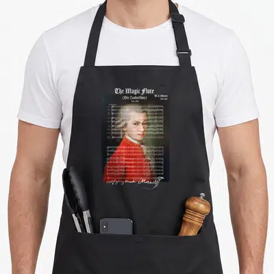 Tablier de cuisine noir avec portrait de Mozart et partition musicale The Magic Flute imprimés en blanc et rouge.