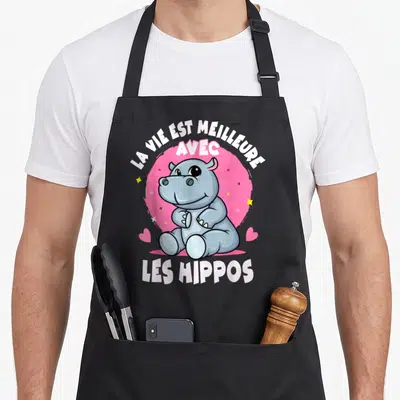 Tablier de cuisine noir avec un hippopotame gris assis devant un cercle rose et des étoiles jaunes.