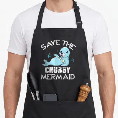Tablier de cuisine noir avec un phoque bleu stylisé et le texte blanc Save the Chubby Mermaid imprimé au centre.