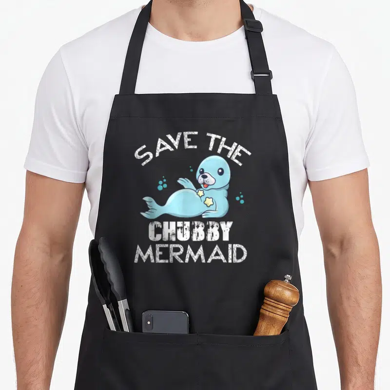 Tablier de cuisine noir avec un phoque bleu stylisé et le texte blanc Save the Chubby Mermaid imprimé au centre.
