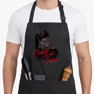 Tablier de cuisine noir avec portrait stylisé femme ponytail et texte rouge Strange is not a Crime NCIS