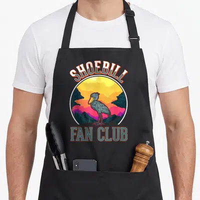 Tablier de cuisine noir avec illustration rétro d'un shoebill devant un ciel coloré et les mots Shoebill Fan Club.