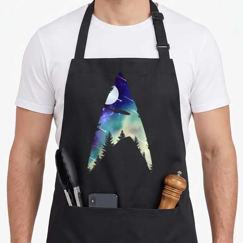 Tablier de cuisine noir avec insigne Starfleet stylisé espace et forêt