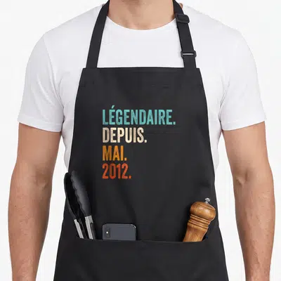 Tablier de cuisine noir avec le texte légendaire depuis mai 2012 imprimé en lettres colorées et texturées au centre.