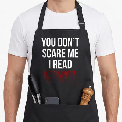 Tablier de cuisine noir avec le texte blanc et rouge You don't scare me I read Creepypasta imprimé au centre.