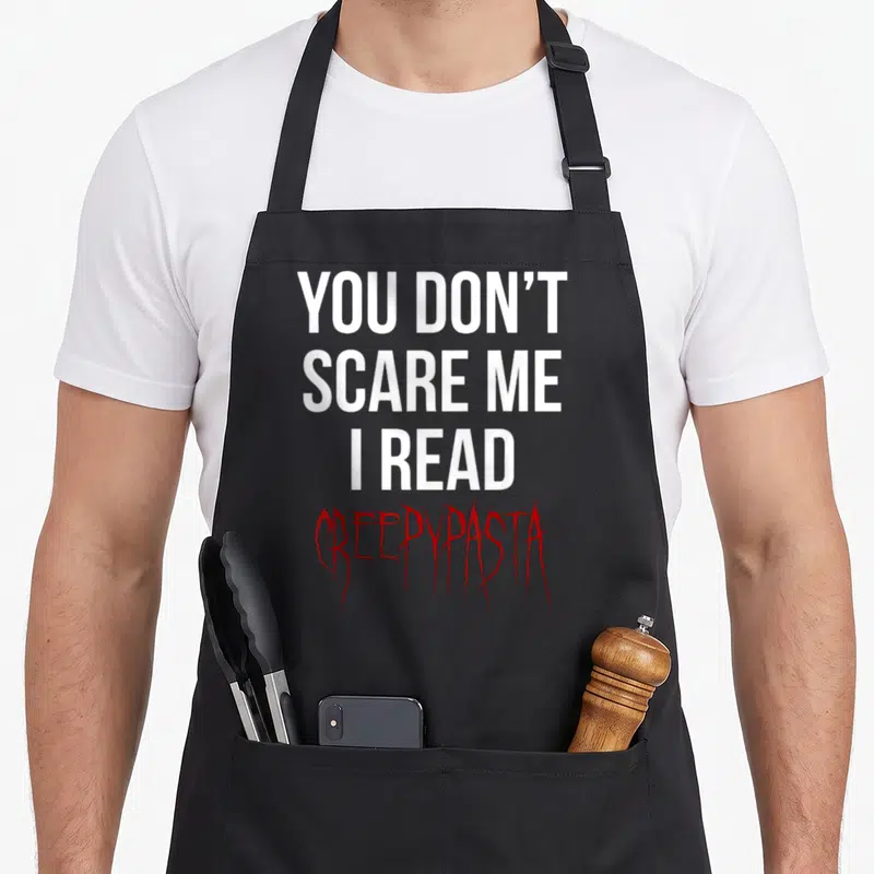 Tablier de cuisine noir avec le texte blanc et rouge You don't scare me I read Creepypasta imprimé au centre.
