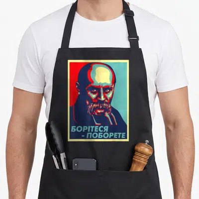 Tablier de cuisine noir avec portrait graphique de Taras Shevchenko et texte en alphabet cyrillique.