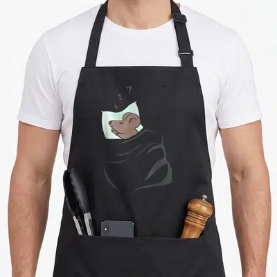 Tablier de cuisine noir avec une souris marron dormant sur un oreiller vert et une couverture grise.