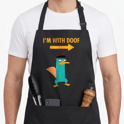 Tablier de cuisine noir avec illustration de Perry le platypus en chapeau et flèche orange pointant vers lui.