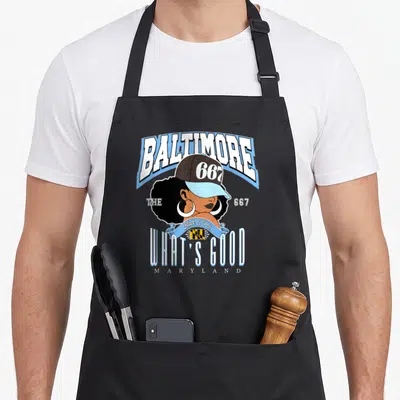 Tablier de cuisine noir avec illustration d'une femme afro puff portant un casque 667 et le texte Baltimore What's Good Maryland.