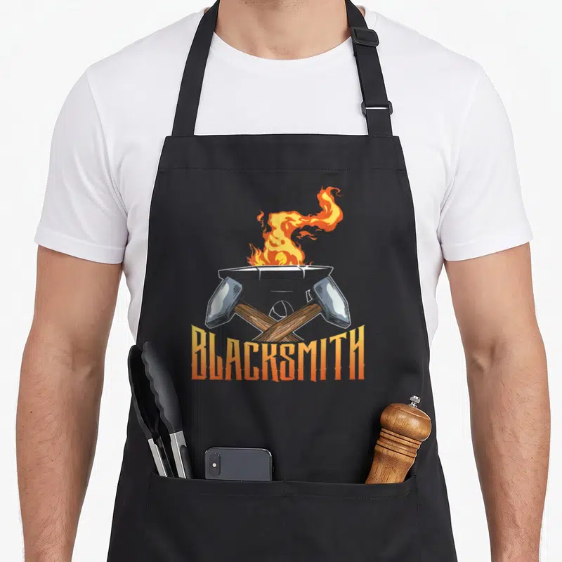 Tablier de cuisine noir avec enclume, deux marteaux croisés et le mot Blacksmith en orange sous un feu stylisé.