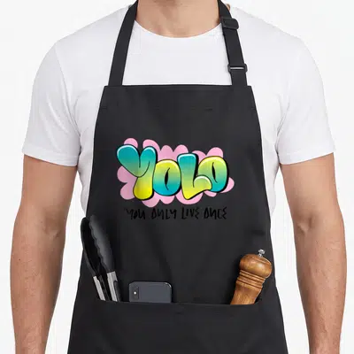 Tablier de cuisine noir avec motif YOLO graffiti bleu jaune sur fond rose et texte You Only Live Once.