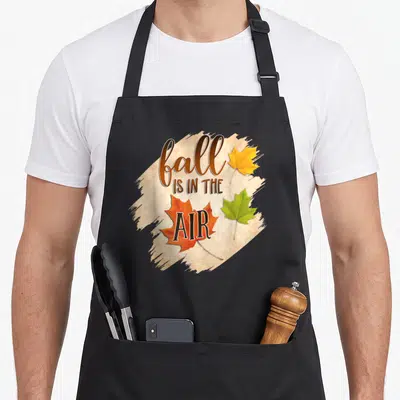 Tablier de cuisine noir avec inscription Fall is in the Air et trois feuilles d'érable jaune orange et vert.