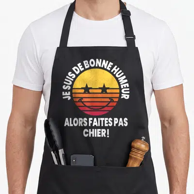 Tablier de cuisine noir avec un logo soleil rétro jaune orange rose et le texte blanc Je suis de bonne humeur faites pas chier.