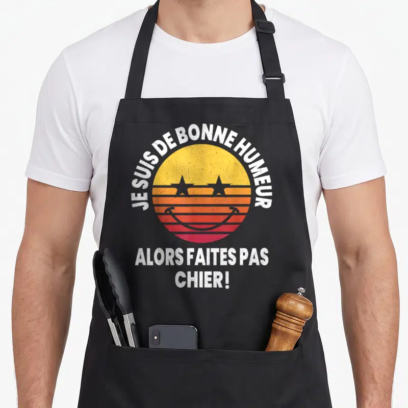 Tablier de cuisine noir avec un logo soleil rétro jaune orange rose et le texte blanc Je suis de bonne humeur faites pas chier.