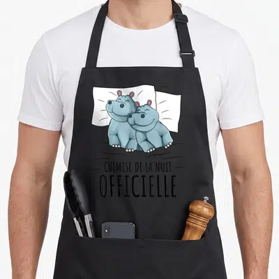 Tablier de cuisine noir avec deux hippopotames souriants sur un oreiller et le texte «chemise de la nuit» imprimé en noir.