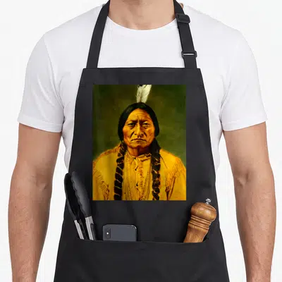 Tablier de cuisine noir avec portrait coloré d'un homme Lakota coiffé d'une plume blanche et vêtu d'une tenue frangée.